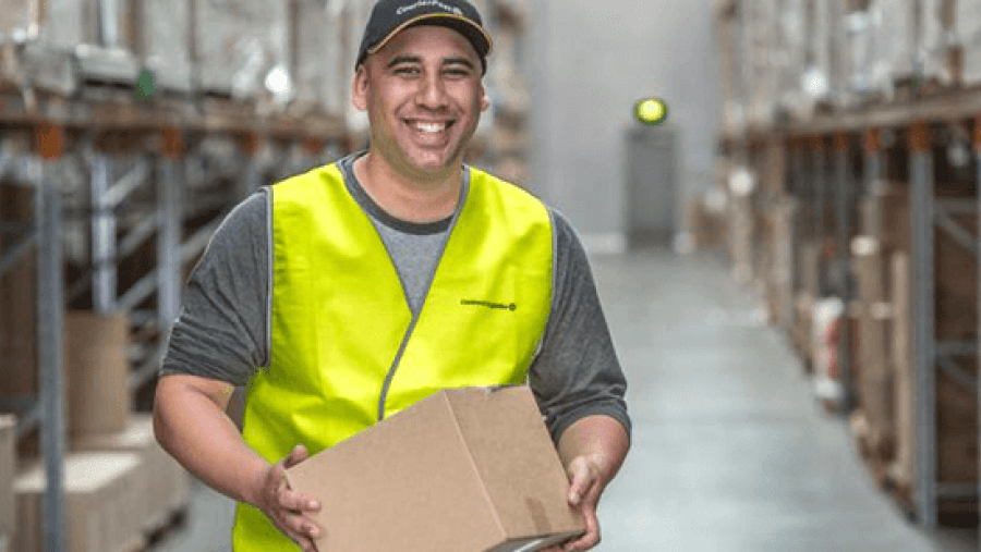 Smiling man in high-vis vest holding box in a warehouse