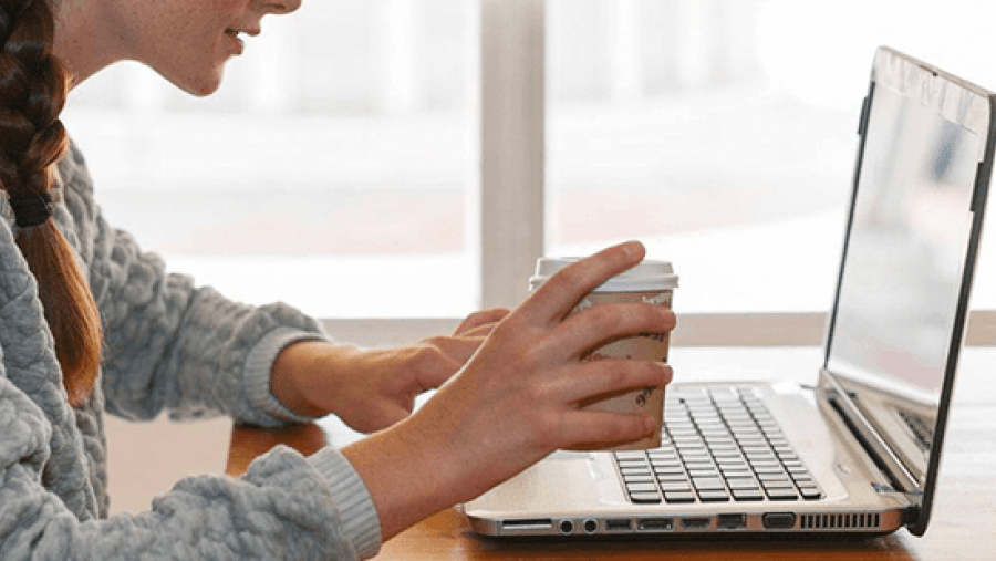 Woman holding a coffee while working on a laptop