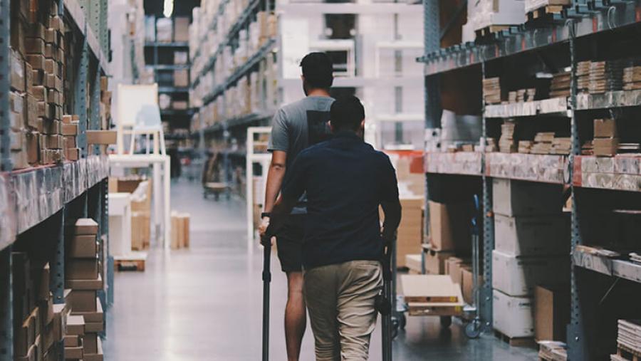 Two men with a trolley walking down a warehouse aisle